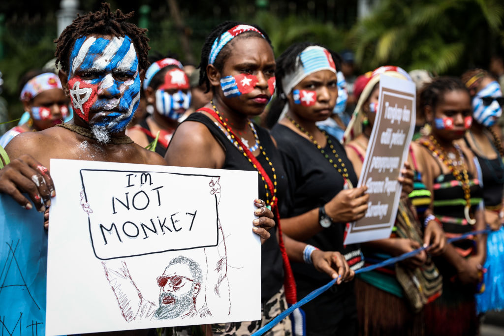 Protesters with West Papua flag painted on their face, holding sign that says I'm not a monkey